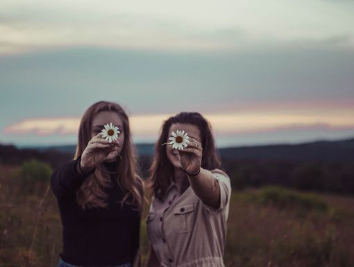 zwei Frauen halten jeweils eine Blüte in die Kamera